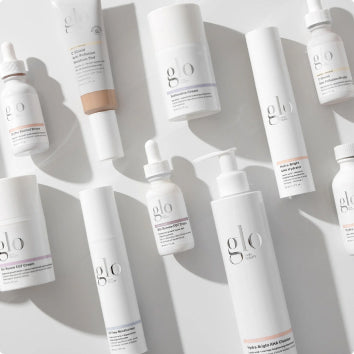 Multiple white skincare product bottles and tubes from the brand glo arranged on a light surface.