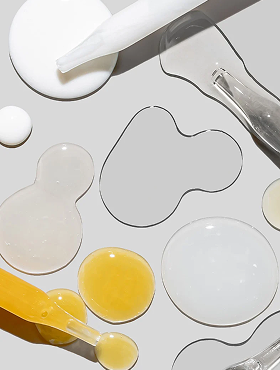Various serum droplets and glass droppers—clear, milky, and yellow liquids—arranged on a light gray background.